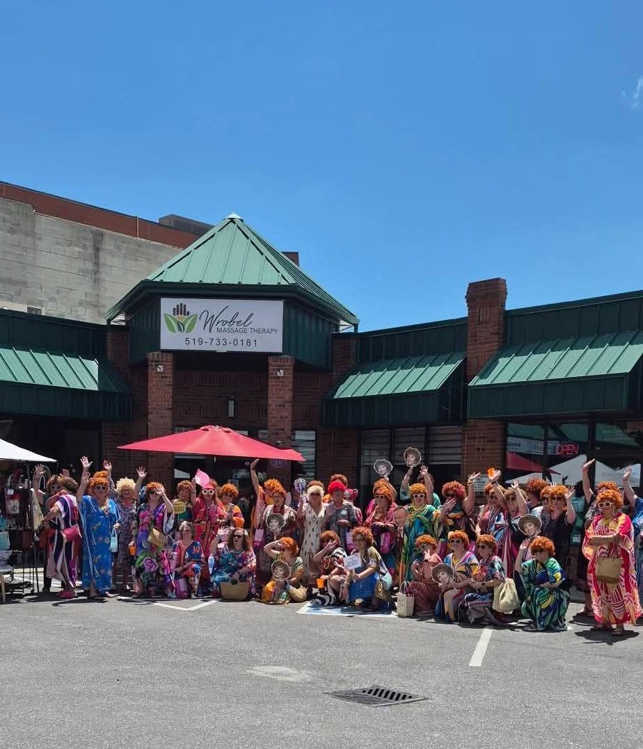 A group of women dressed in vibrant caftans and colorful accessories for the Mrs. Roper's Romp event outside Wrobel Massage Therapy.